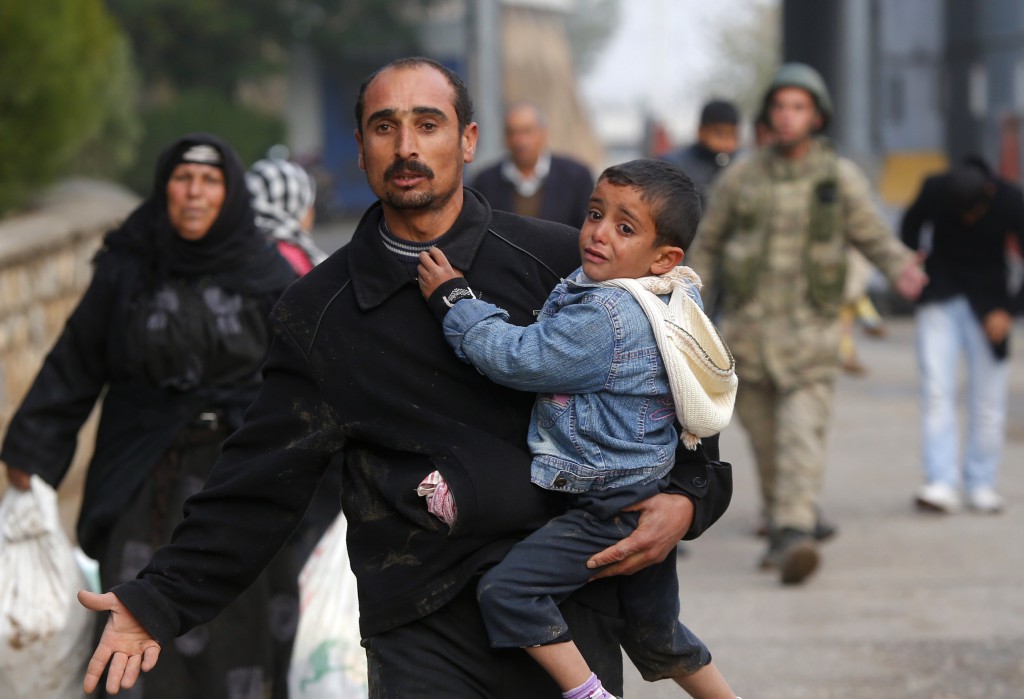 A Syrian man carries a child as displaced people cross the border from the Syrian town of Ras al-Ain to the town of Ceylanpinar, Turkey. PHOTO: CNS/Laszlo Balogh, Reuters