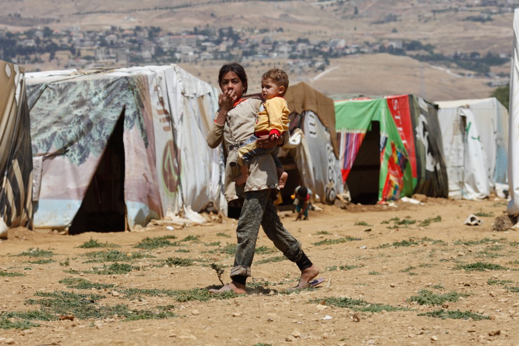 Mohammad, 11 months old, is carried by his sister across an informal refugee settlement in late July. PHOTO: CNS/Sam Tarling, Catholic Relief Services