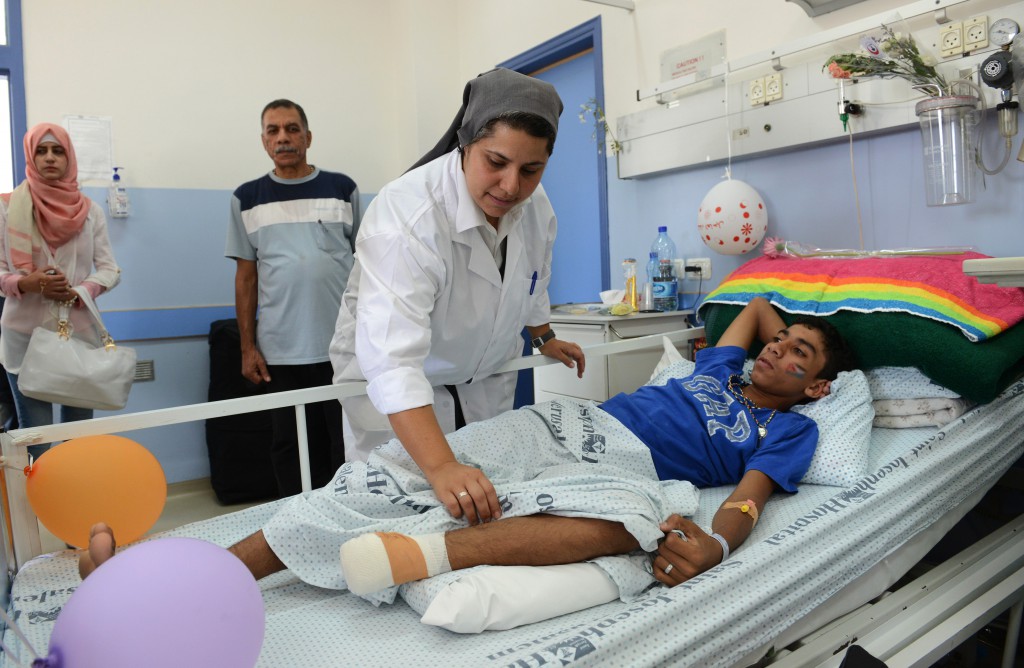 Sister Muna Totah, a member of the Sisters of St. Joseph of the Apparition, works on Karim Nofal, 15, of  Gaza, at St. Joseph Hospital in Jerusalem July 30. The teenager is one of 23 Gaza patients being treated at the hospital, which specializes in head- and chest-trauma wounds. PHOTO: CNS/Debbie Hill