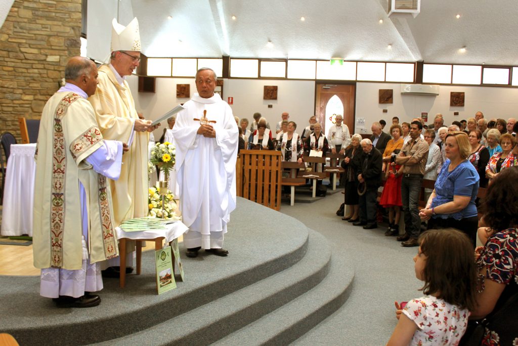 Auxiliary Bishop Donald Sproxton blesses the 60th anniversary history books at the special Mass on 23 October next to Parish Priest, Francis Ly, and Permanent Deacon Trevor Lyra. Photo Supplied