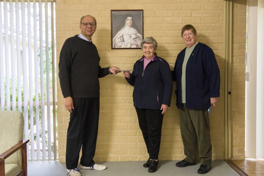 Musical director of the Julian Singers Chris deSilva presents a cheque for $2,800, the remainder of the dissolved choir’s funds to Sister Naomi McClements and Sr Catherine O’Connor, members of ACRATH in WA. Photo: Caroline Smith.