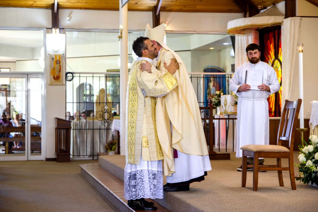 Newly ordained Deacon Chris de Sousa is embraced by Bishop Don Sproxton, moments after his parents placed a chasuble over his garments for the very first time. Photo: Matthew Lau.