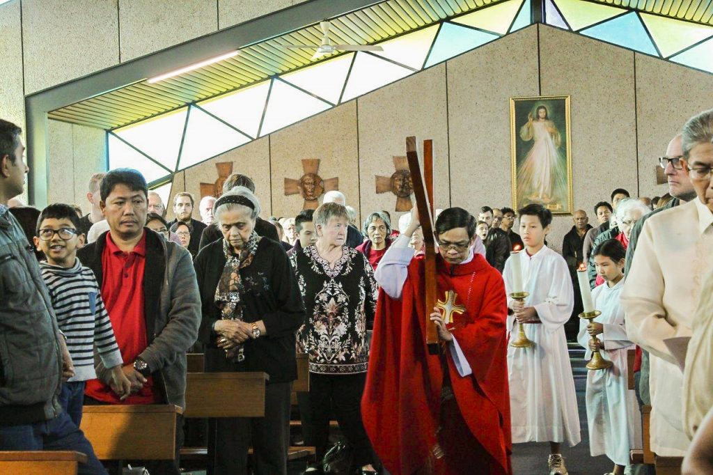 Fr Quynh carries a cross down the aisle during the Lord’s Passion. Photo: Sunil Rodrigues.