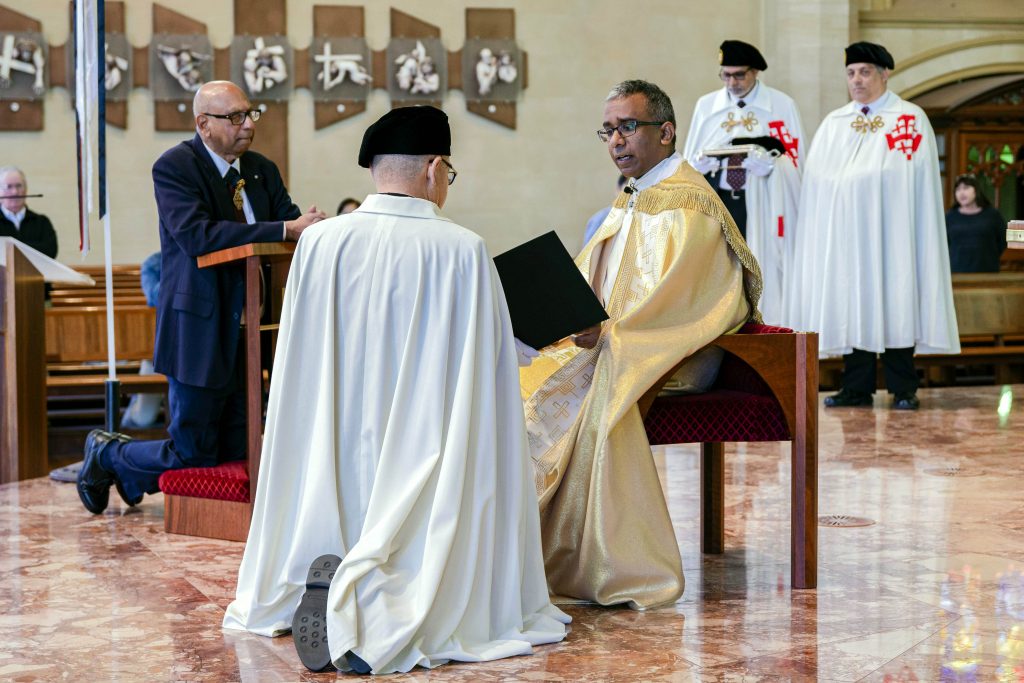 Keven Susai KCHS and Incumbent Lieutenant Jack Gardner KCHS kneel before the Altar at St Mary’s, addressed by Cathedral Dean Fr Sean Fernandez. Photo: Eric Martin.